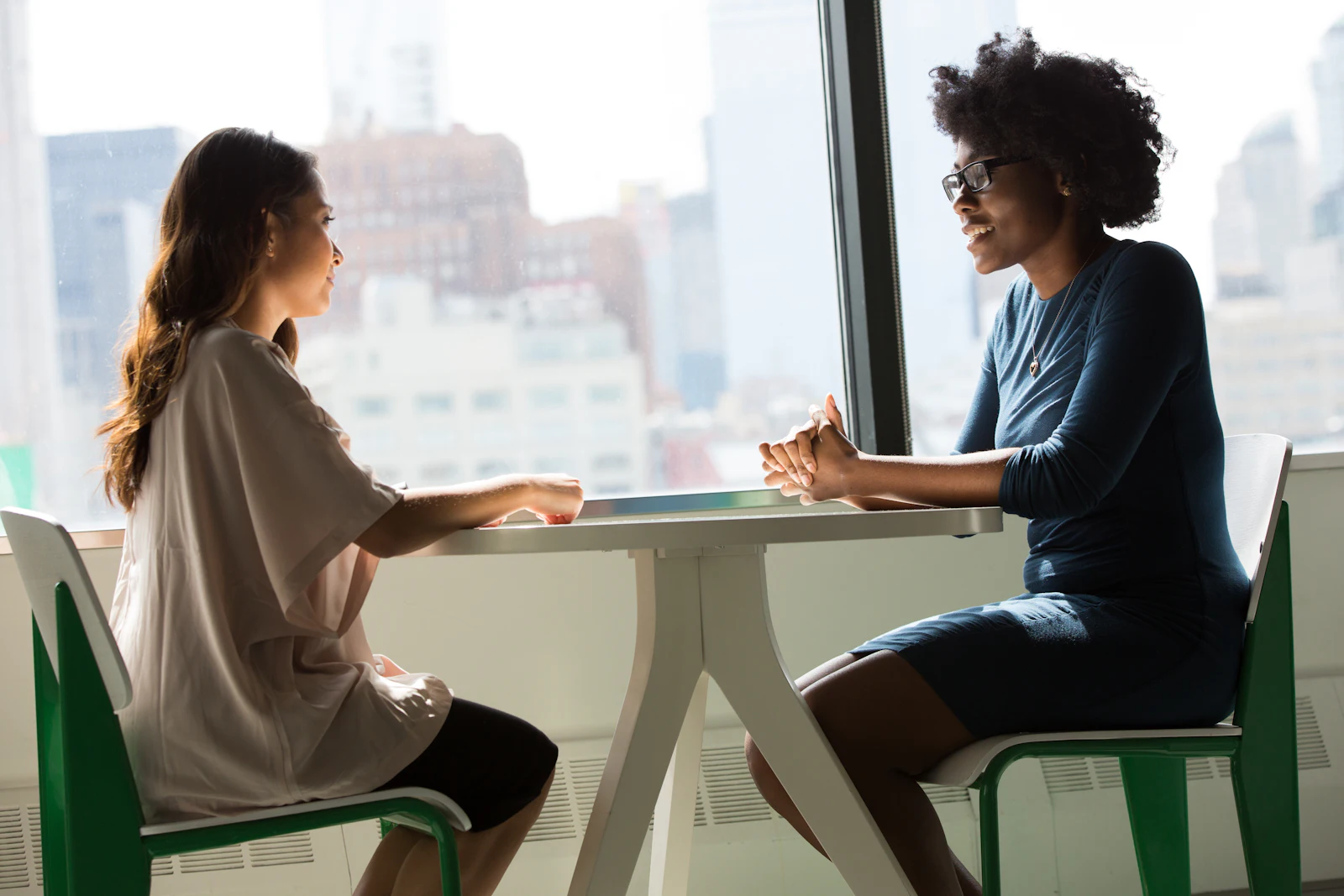 Two professionals in conversation at a table by a bright window